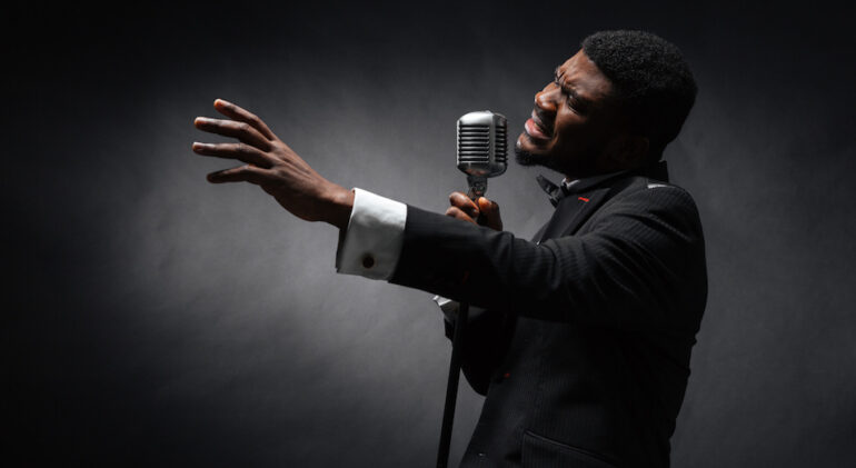 Afro amerian man singing into vintage microphone over dark background