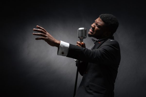 Afro amerian man singing into vintage microphone over dark background